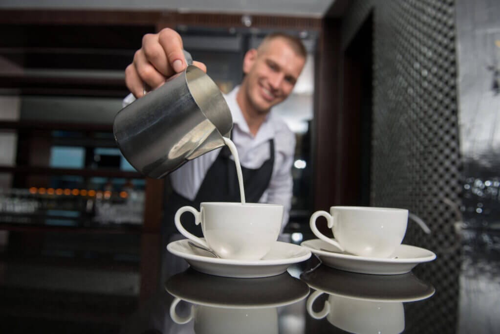 Barista am Milchschaum einschenken mit 2 Tassen